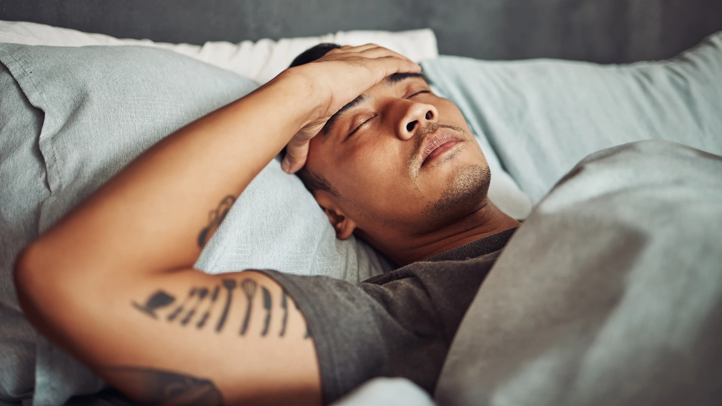 A man clutches his forehead as he lies in bed.