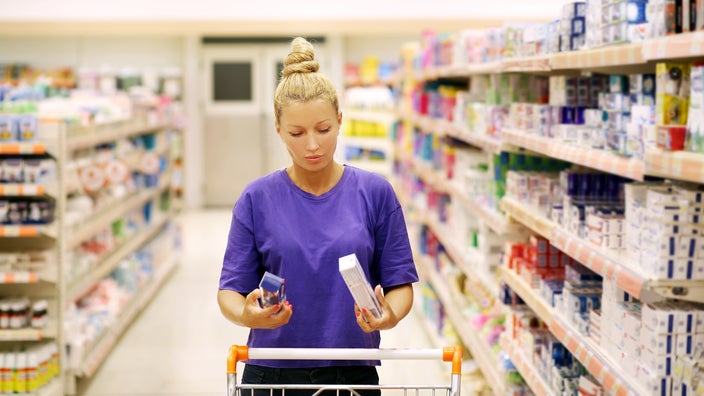 Woman reading product information in shopping aisle.