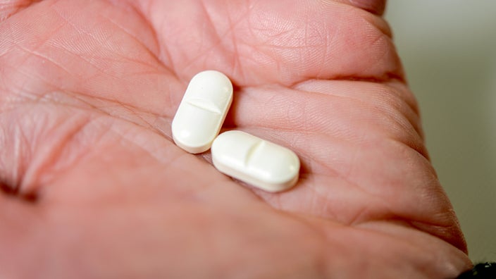 Two white oblong pills sit in the palm of a hand. 