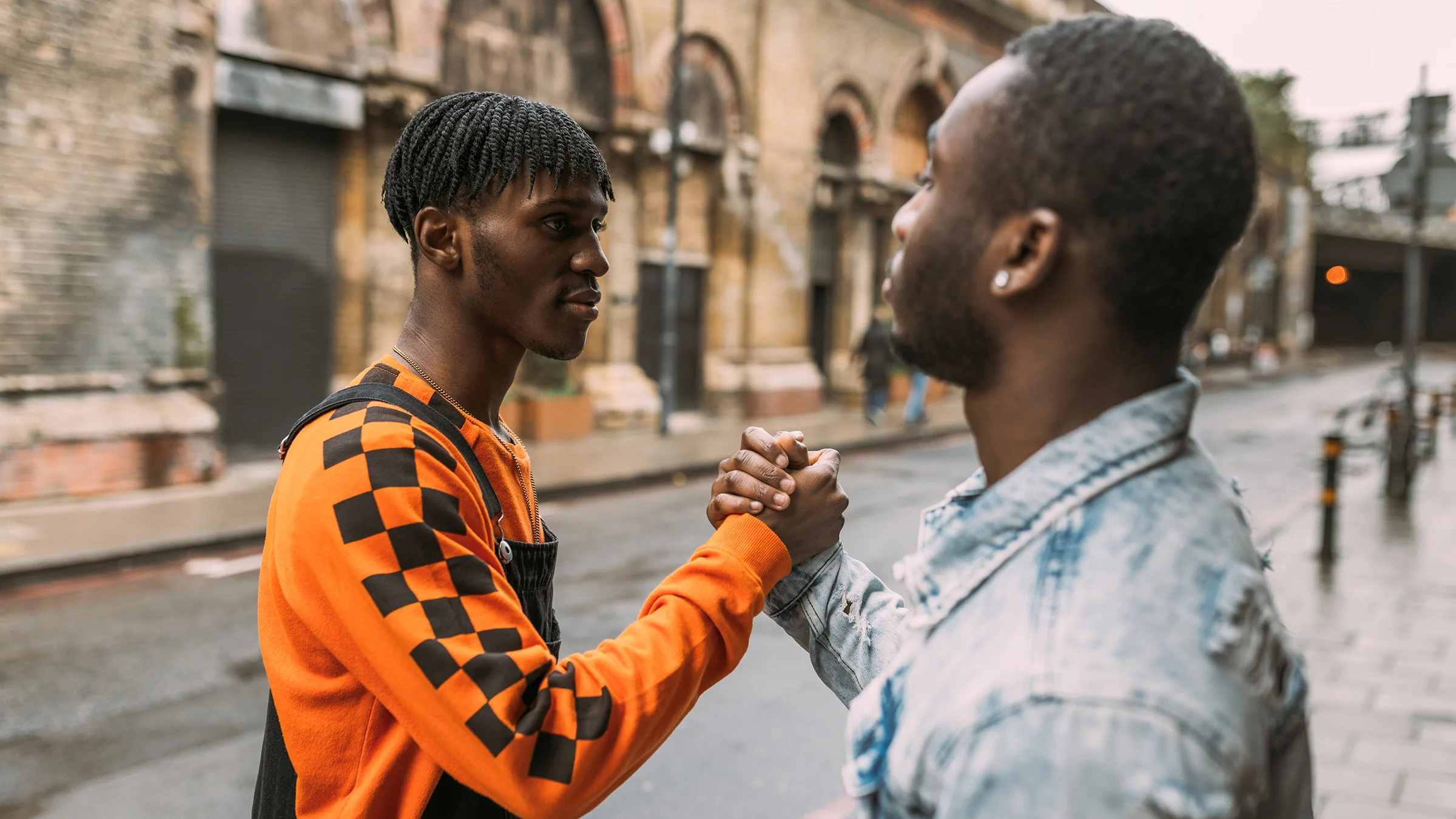 Two friends shake hands outdoors.
