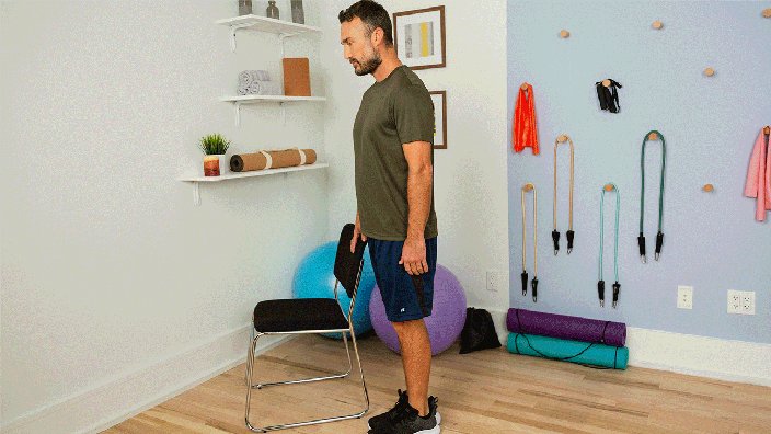 Profile view of man using a chair to balance while lifting the other leg to stretch quadricep.