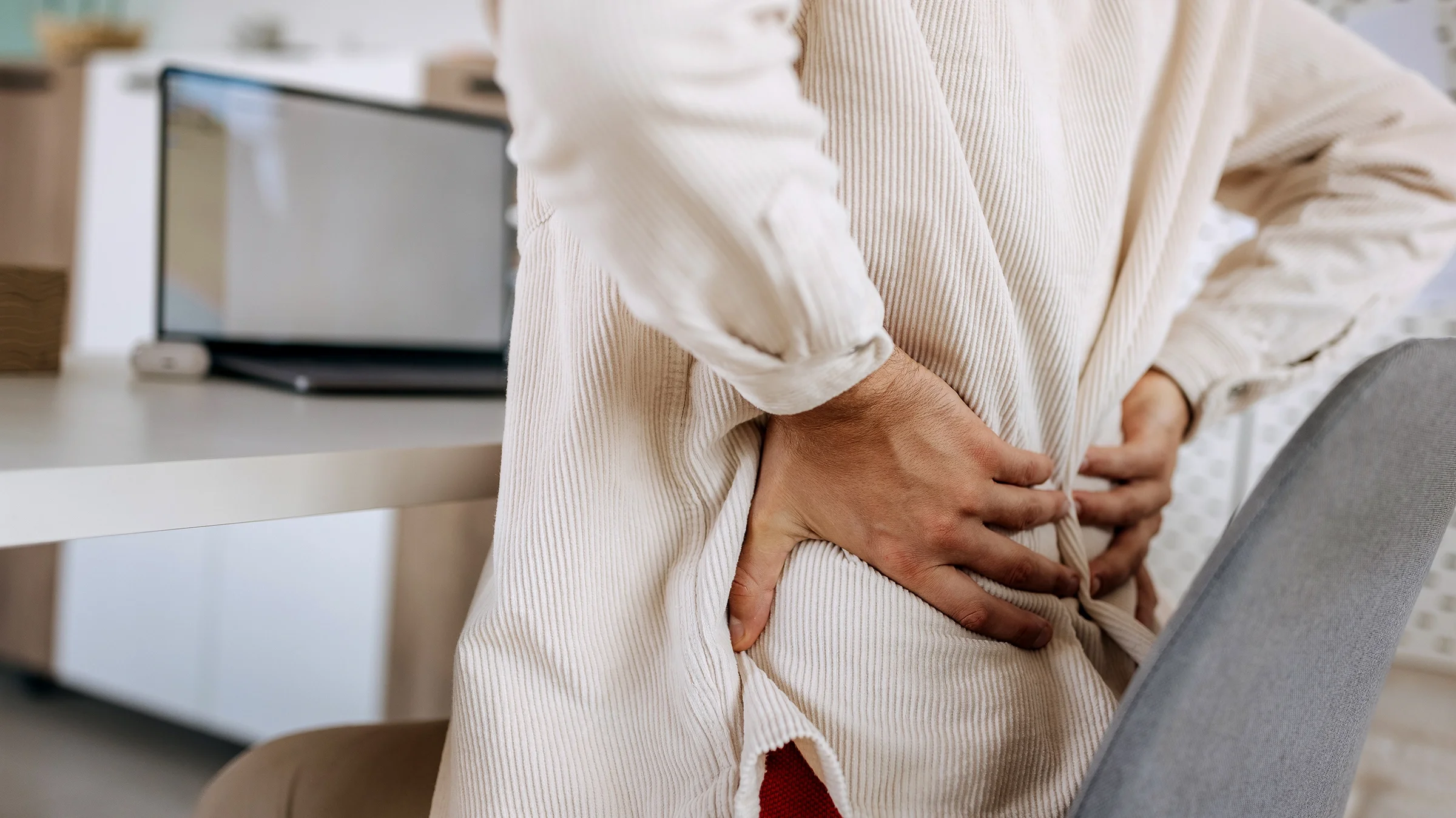 A person grabs their lower back as they experience pain while working at home. 