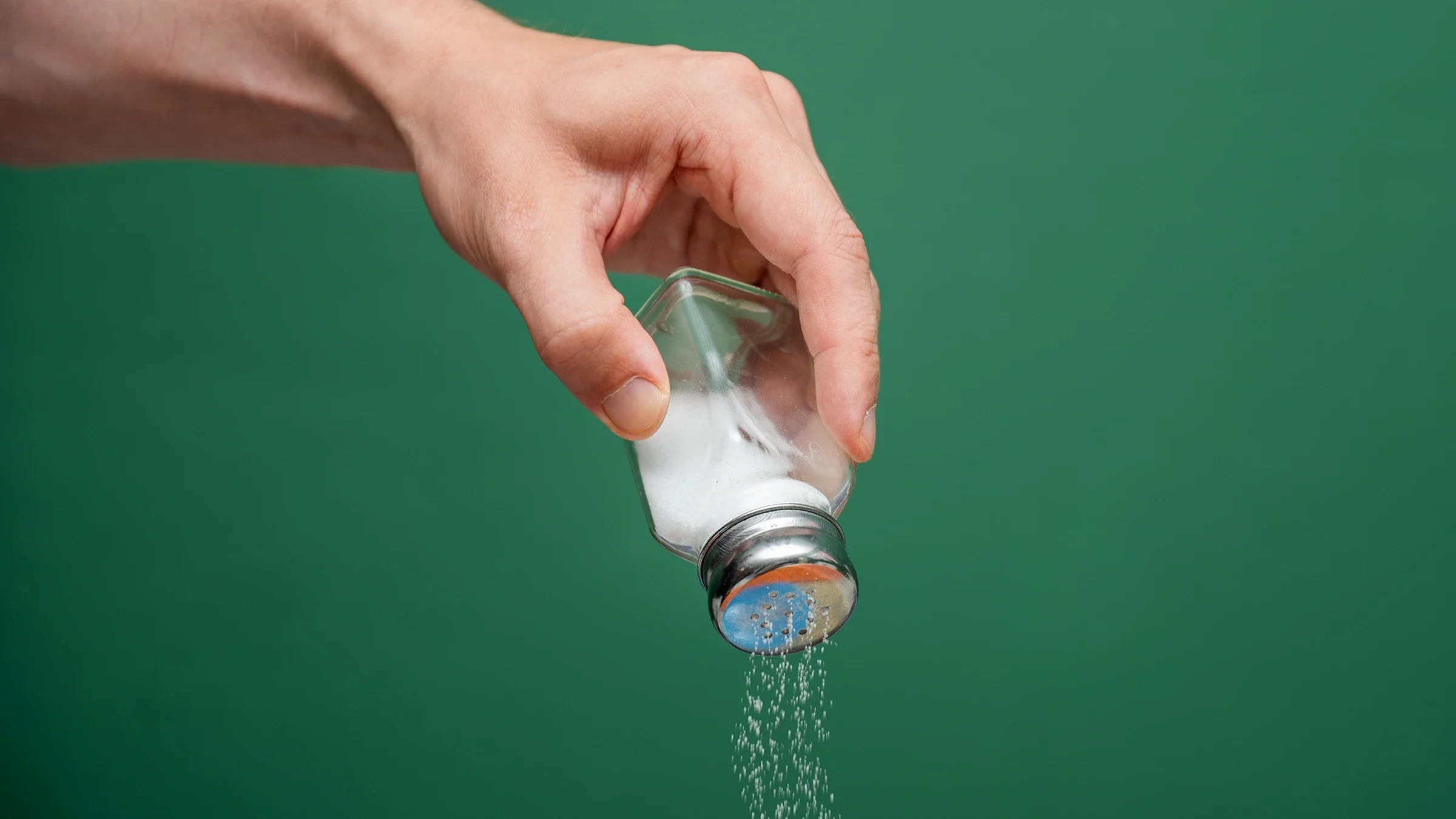 Hand holding a salt shaker against a green background