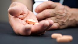 Close-up on an elderly man holding pills in his hand. You can see his other hand in the background out of focus holding the white pill bottle.
Suze777/iStock via Getty Images