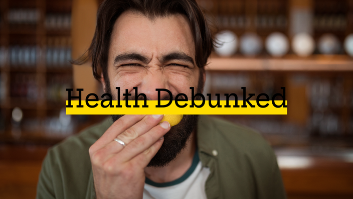 Man eating lemon and squinting from the acidic taste. There is added text on top reading “Health Debunked” with a yellow highlight bar behind it.