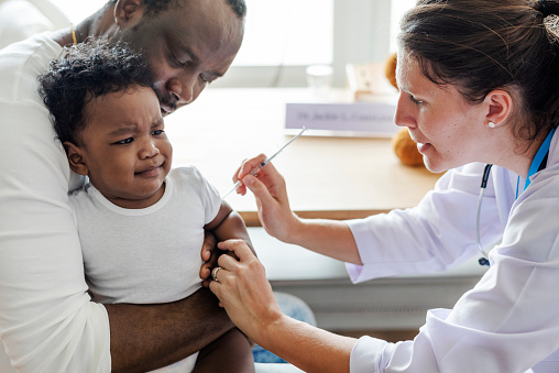 Father holding his baby as they give him his first vaccine from the doctor.
