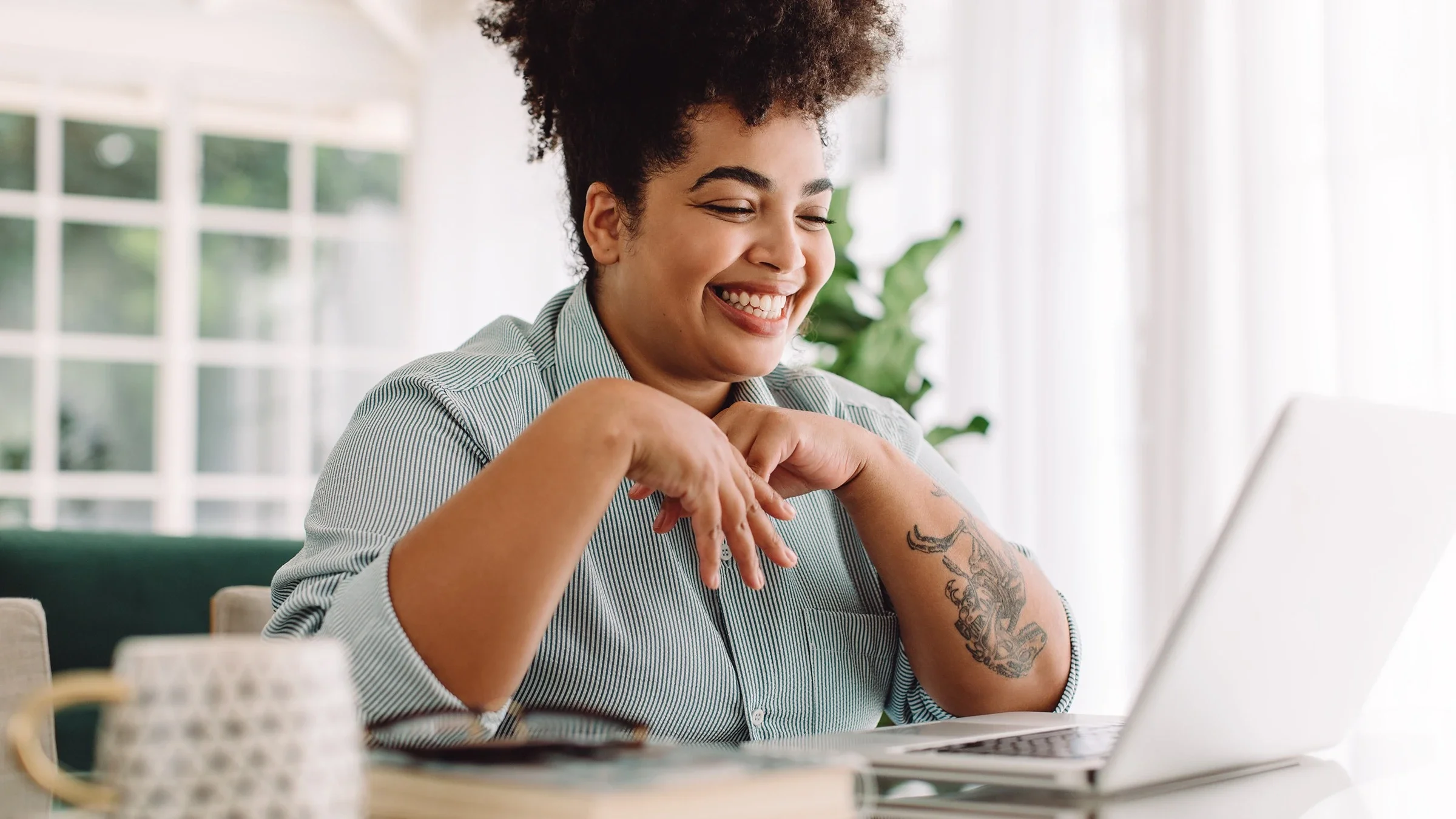 Young woman with curly hair up high on her head smiling big as she talks to someone on video chat on her laptop.