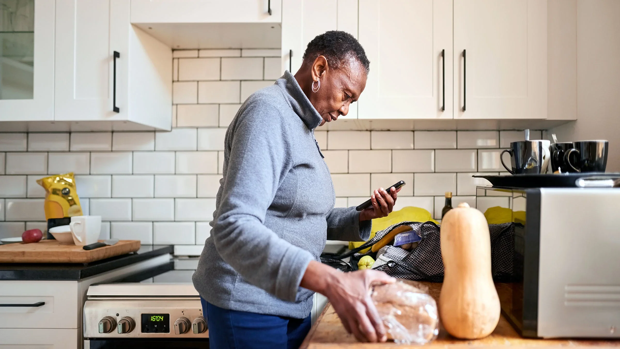 A senior woman uses a mobile phone while unpacking groceries in the kitchen.
AJ_Watt/E+ via Getty Images