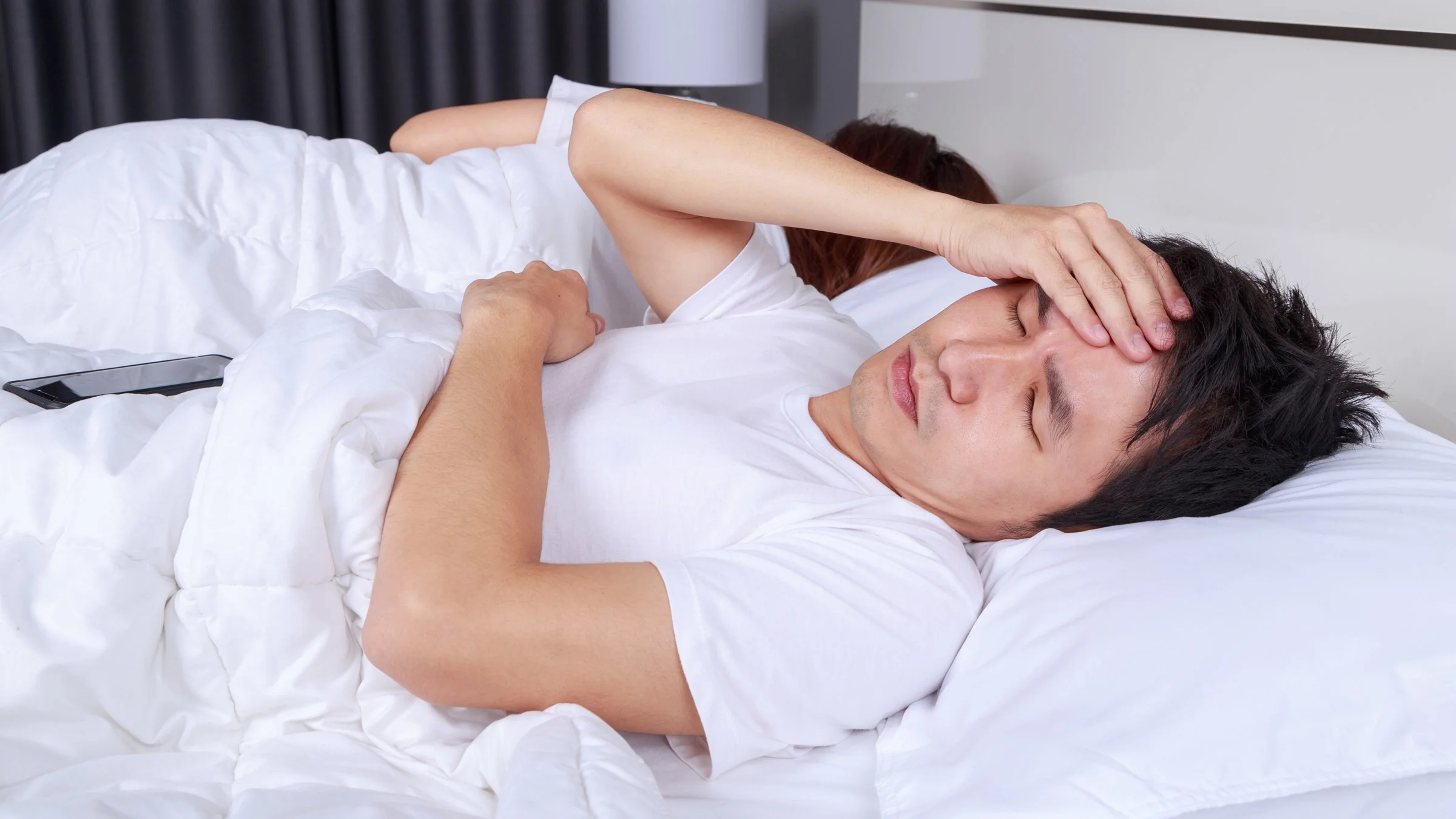 A man with a headache in bed next to his partner.