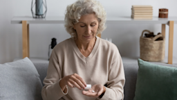 Older woman sitting on couch taking her medicine.
fizkes/iStock via Getty Images