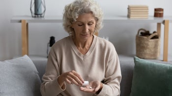 metformin: senior: pills: prescription: older woman taking white pill couch at home-1218234441