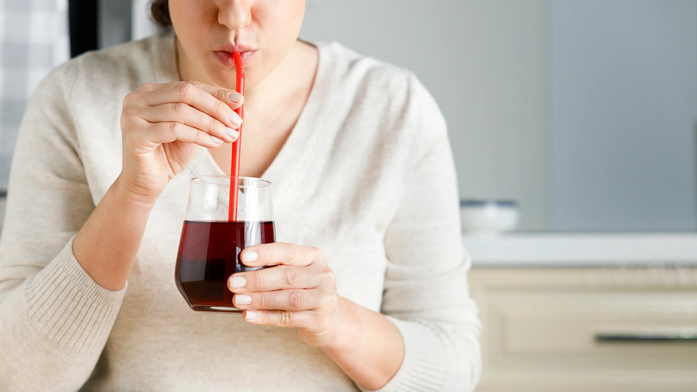 A woman drinks a glass of pomegranate juice.