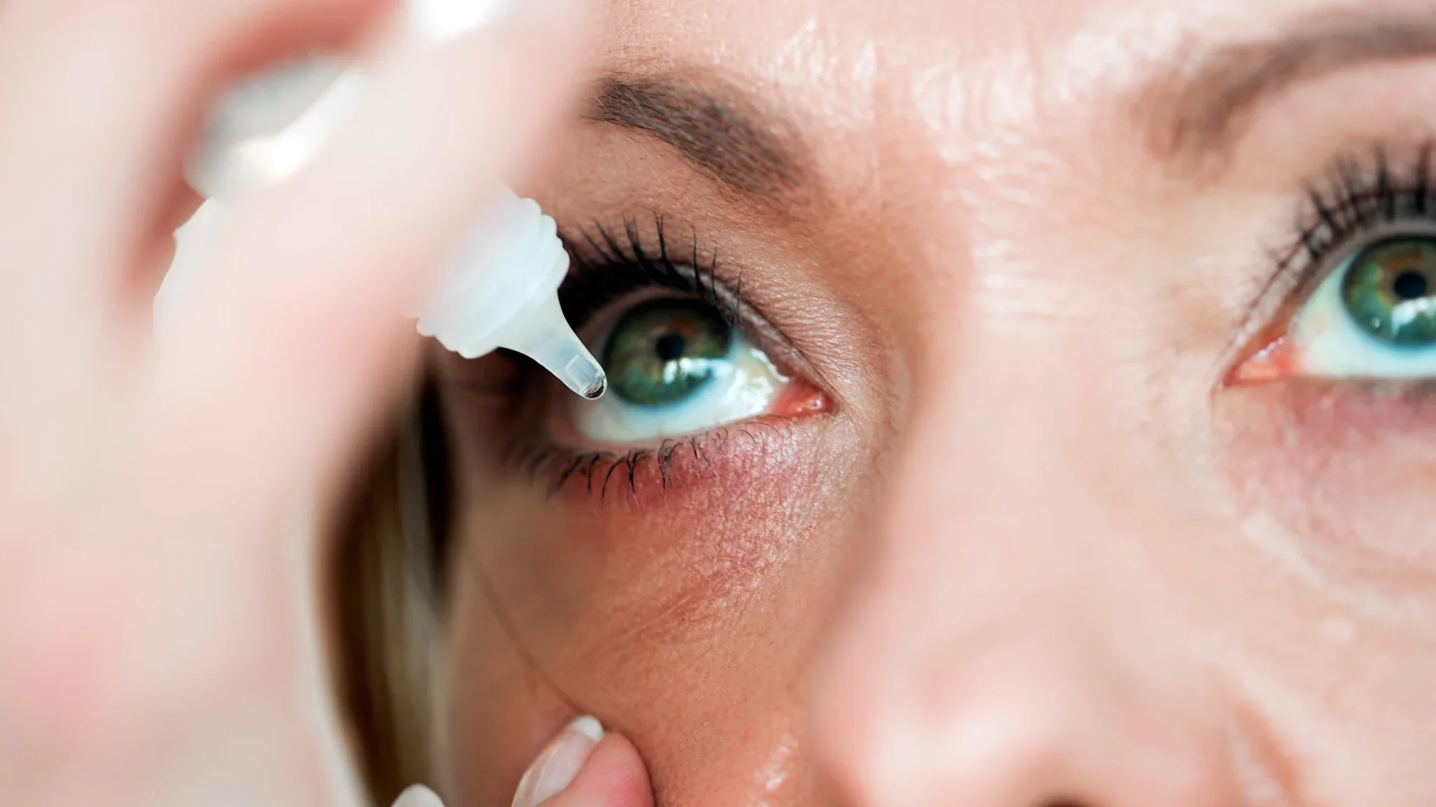 A person is applying eye drops in a close-up.