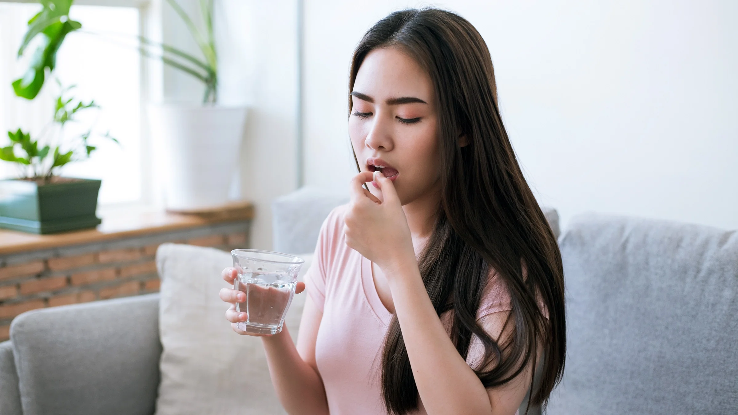 A woman takes medication while sitting on the sofa at home.