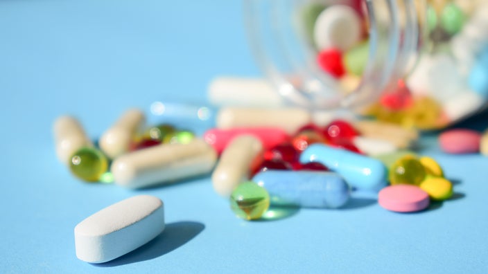 Colorful pills spilling out of the bottle on a light blue background.