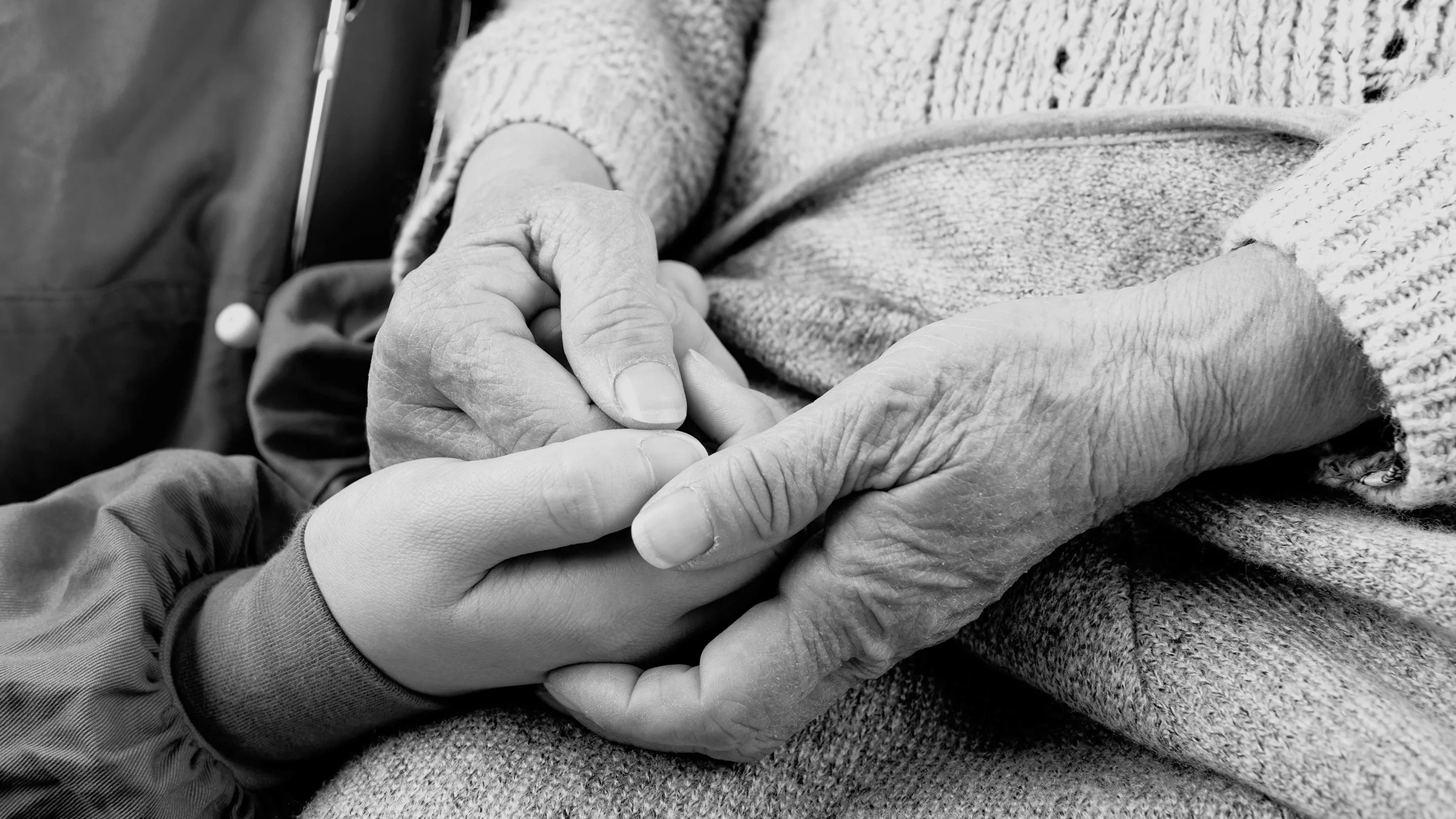 Black and white close-up of a nursing assistant holding a patient's hands to comfort them.