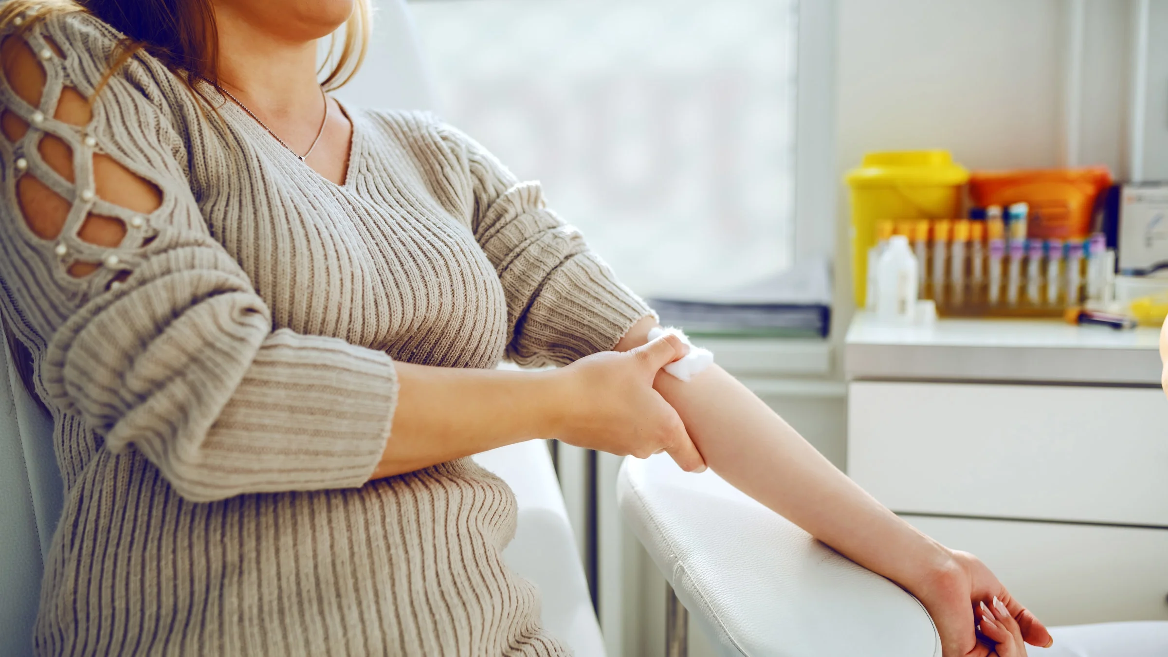 An adult is holding a cotton ball to their arm after having blood drawn.