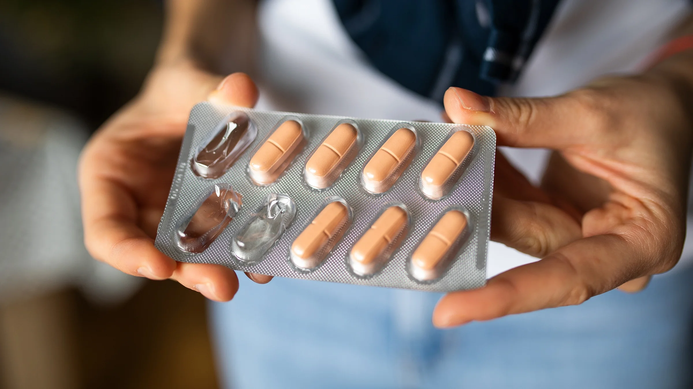 Close-up on a woman holding a blister pack of oblong pink-ish pills.