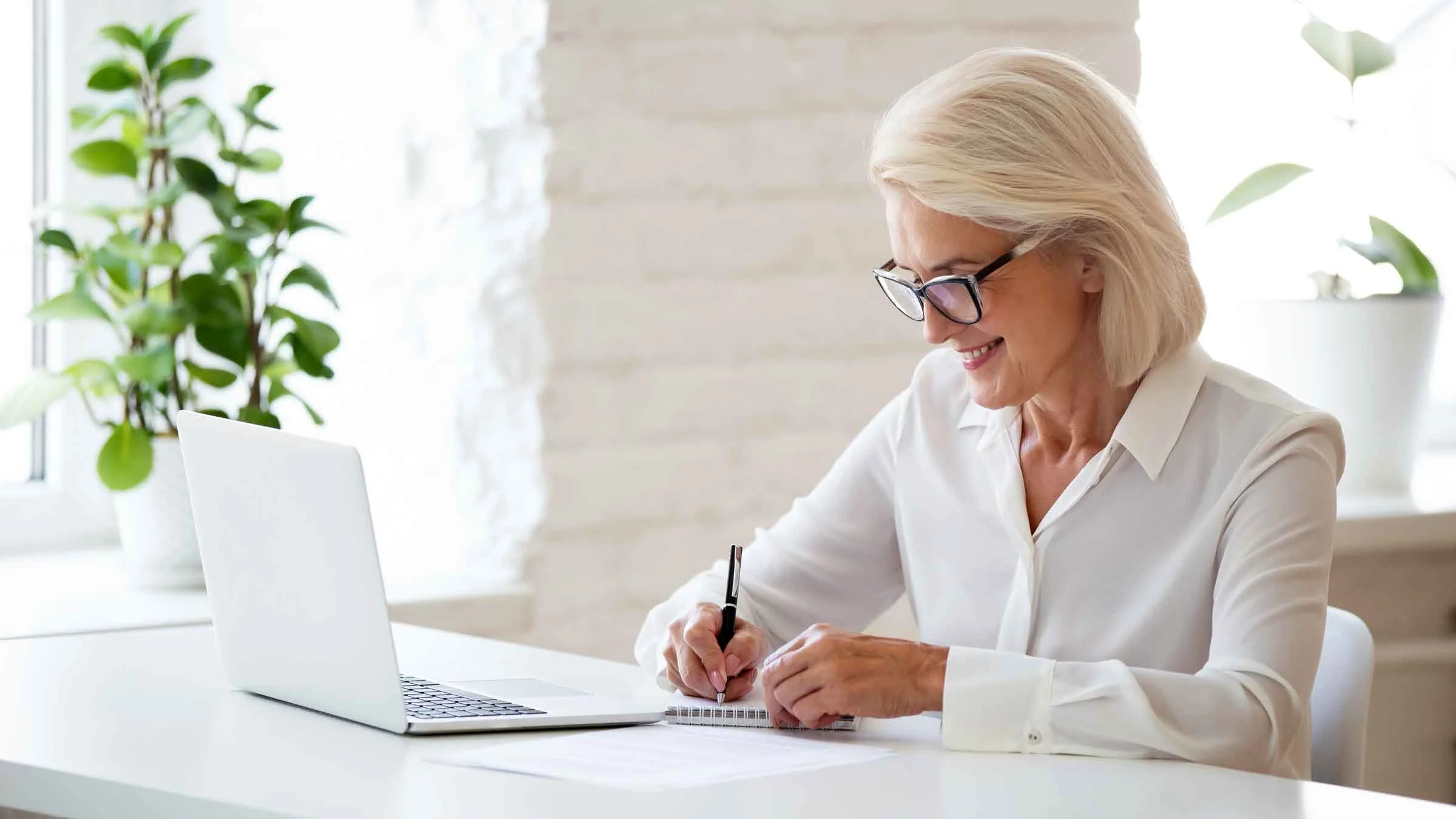 A woman sitting at a desk writes on a notepad.