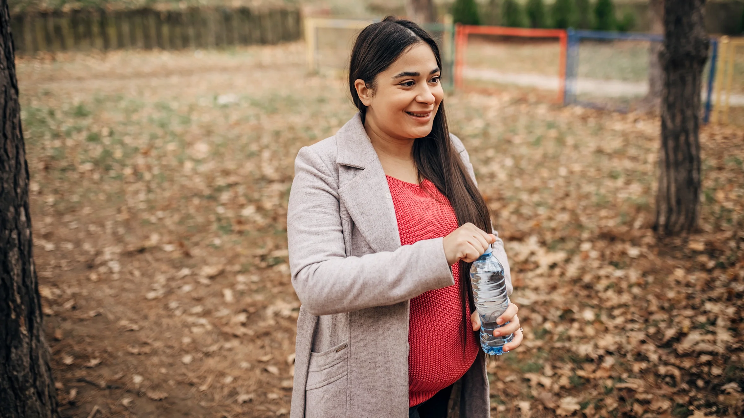 A pregnant woman is drinking bottled water outside.