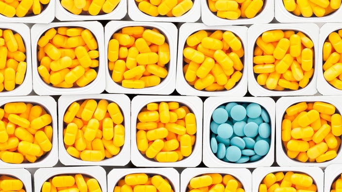 White boxes filled with piles of yellow pills filling the screen. One of the boxes is filled with light blue pills in the bottom right part of the frame.