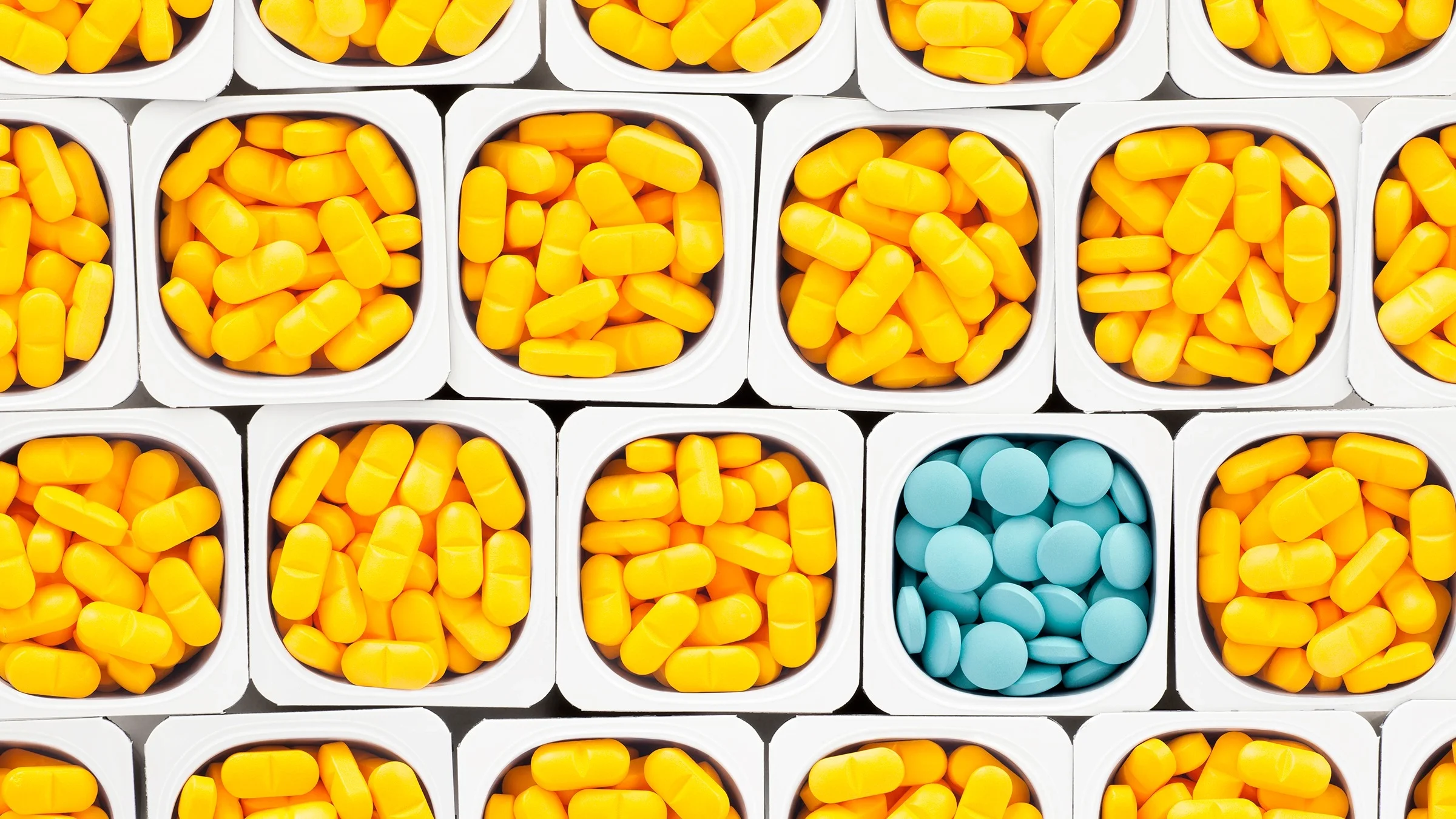 White boxes filled with piles of yellow pills filling the screen. One of the boxes is filled with light blue pills in the bottom right part of the frame.