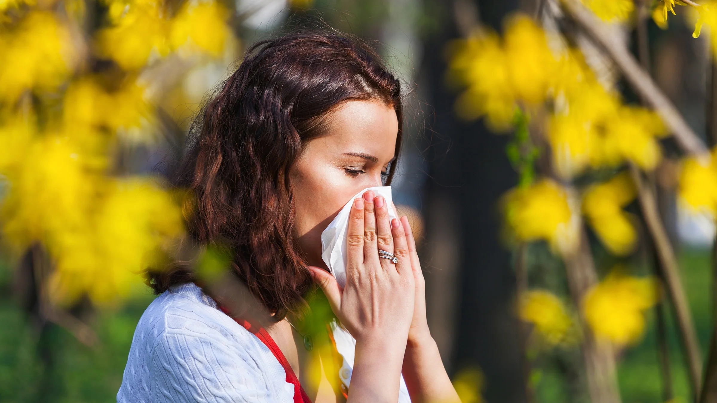 A woman blows her nose while outside at the park.