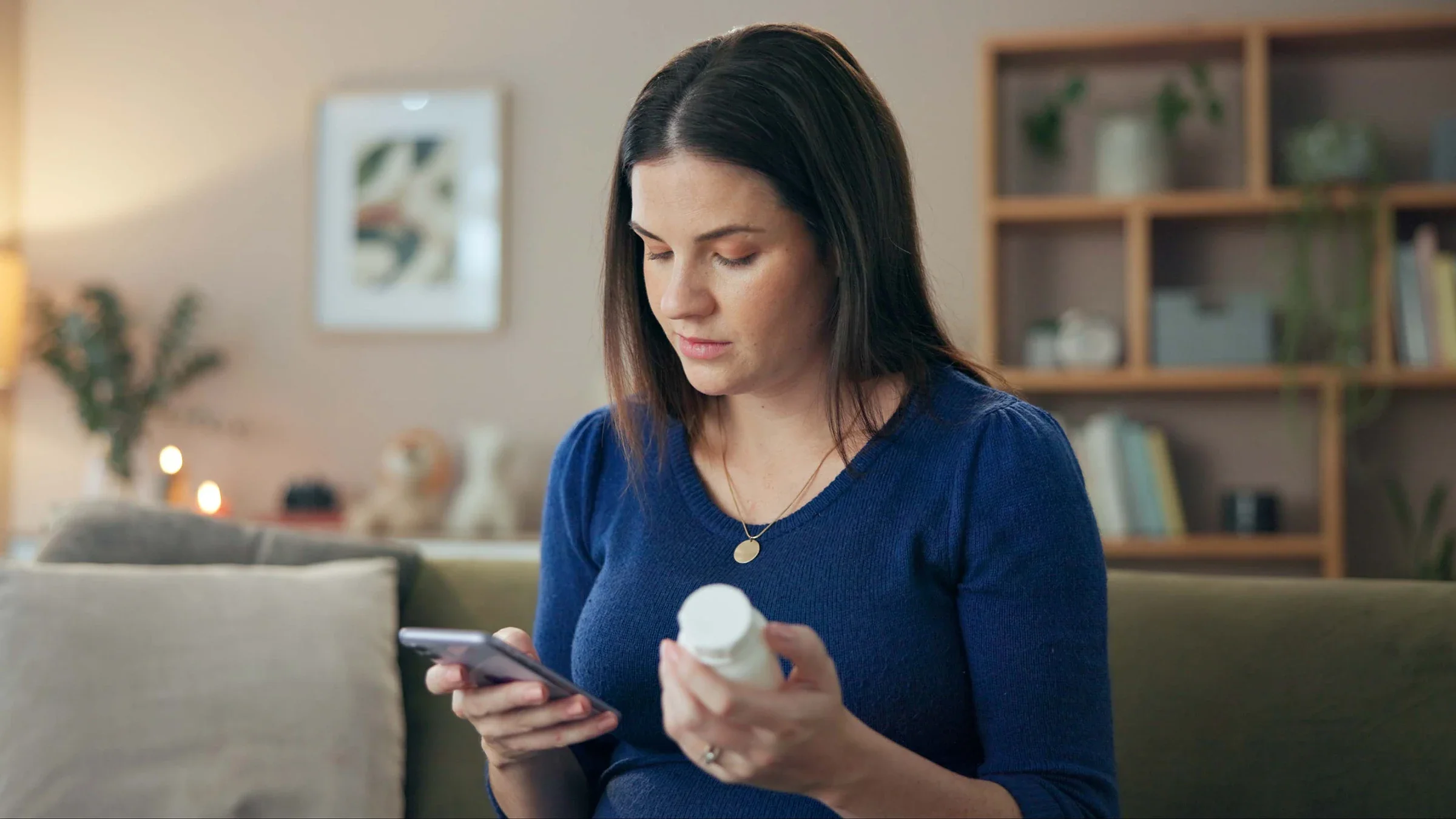 A woman looks at her phone while holding a bottle of vitamins.
Jacob Wackerhausen /iStock via Getty Images Plus