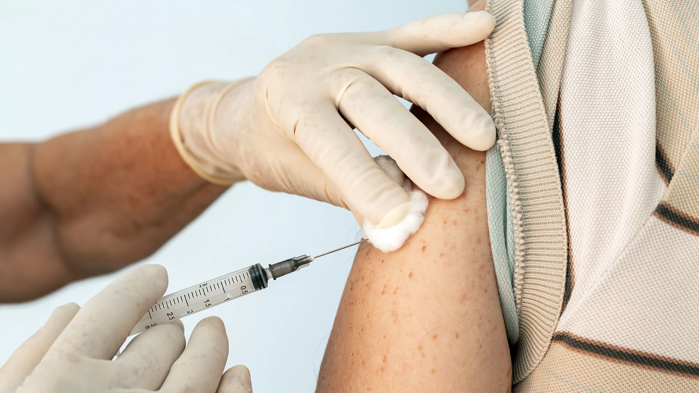 Close-up of a doctor giving a vaccine shot to an older patient while applying a cotton swab to the injection site.