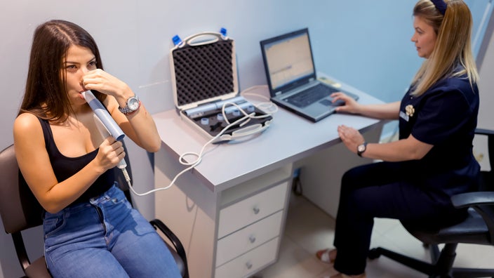 A person is doing a breathing test with a pulmonary device and the help of a healthcare provider.