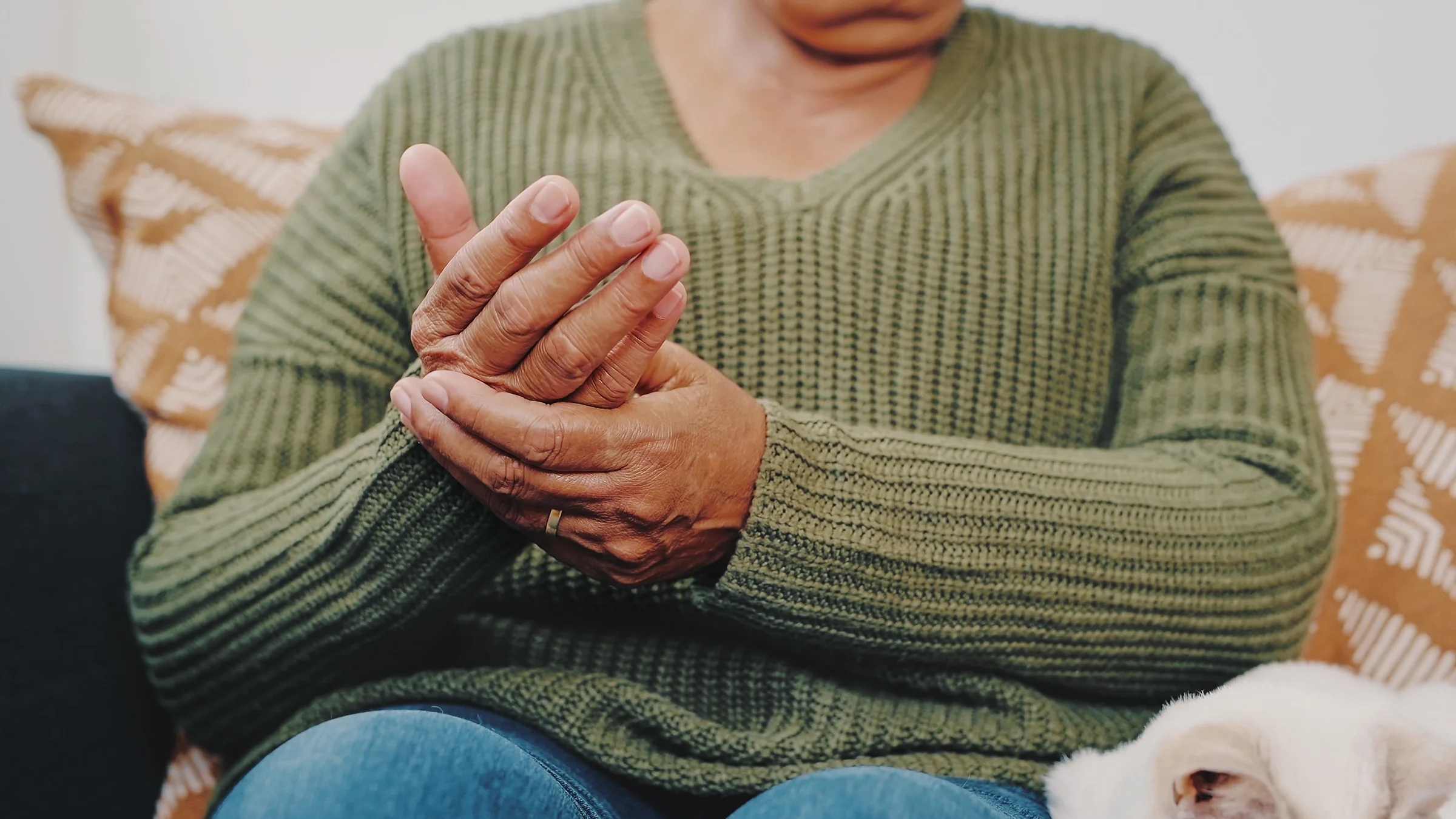 Cropped shot of an adult in a green sweater rubbing their hand as if in pain.