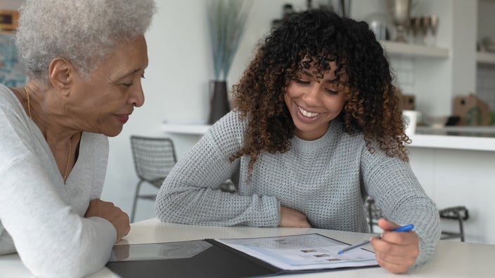 Young woman with curly hair helping an elderly woman review health insurance plans.