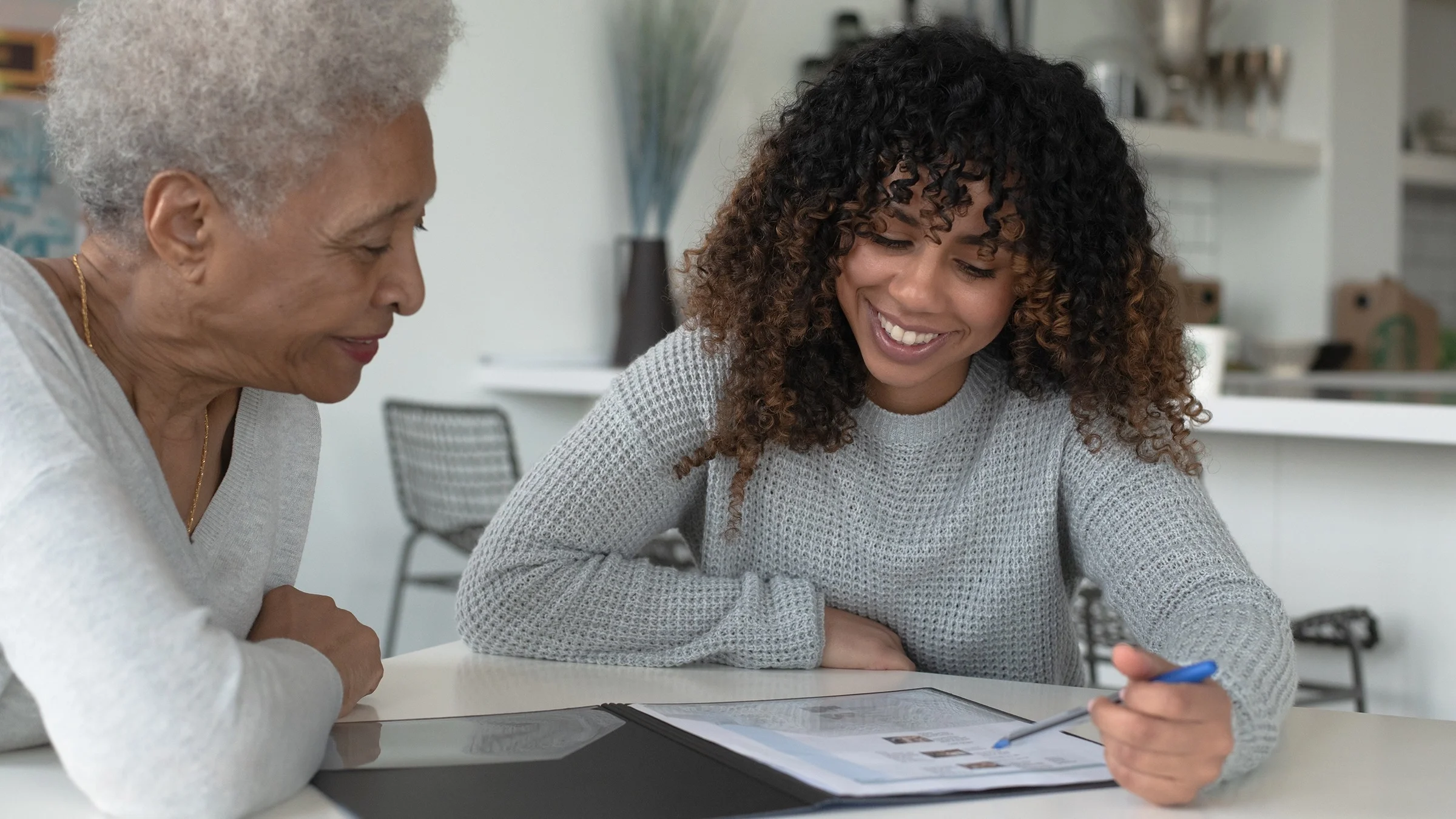 Young woman with curly hair helping an elderly woman review health insurance plans.