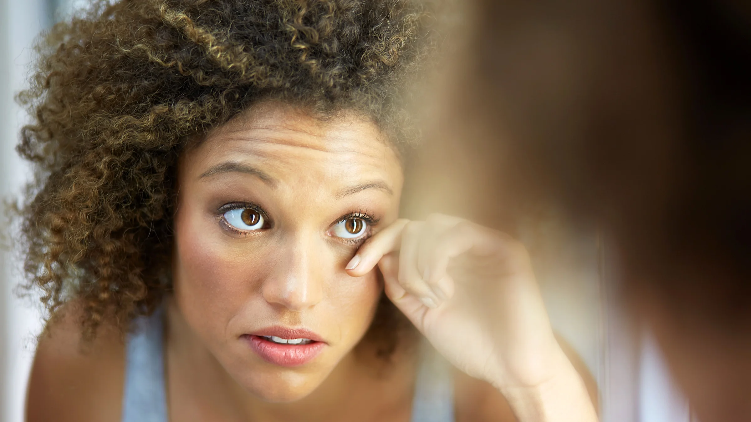 A woman looks at her eyelashes in a mirror.