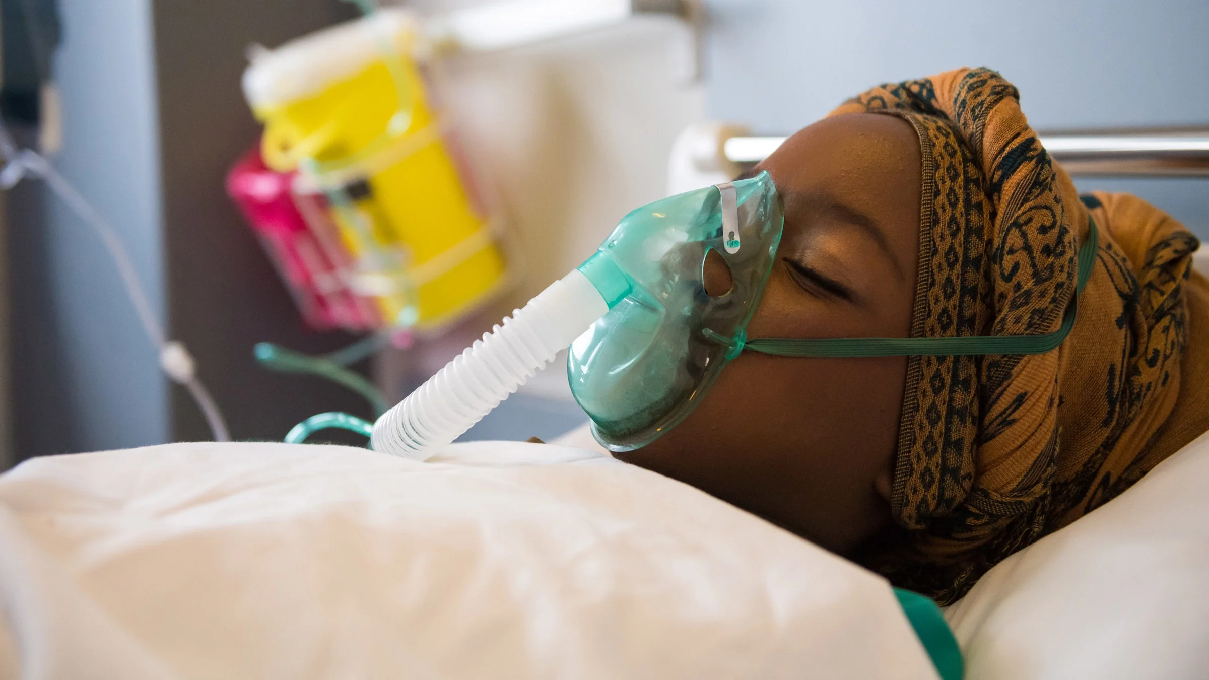 A patient with an oxygen mask in a hospital bed.