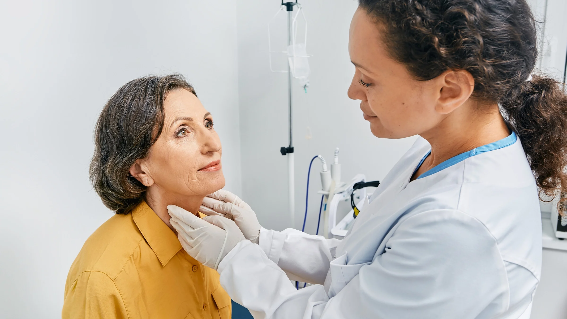 A doctor is checking an older woman’s thyroid.