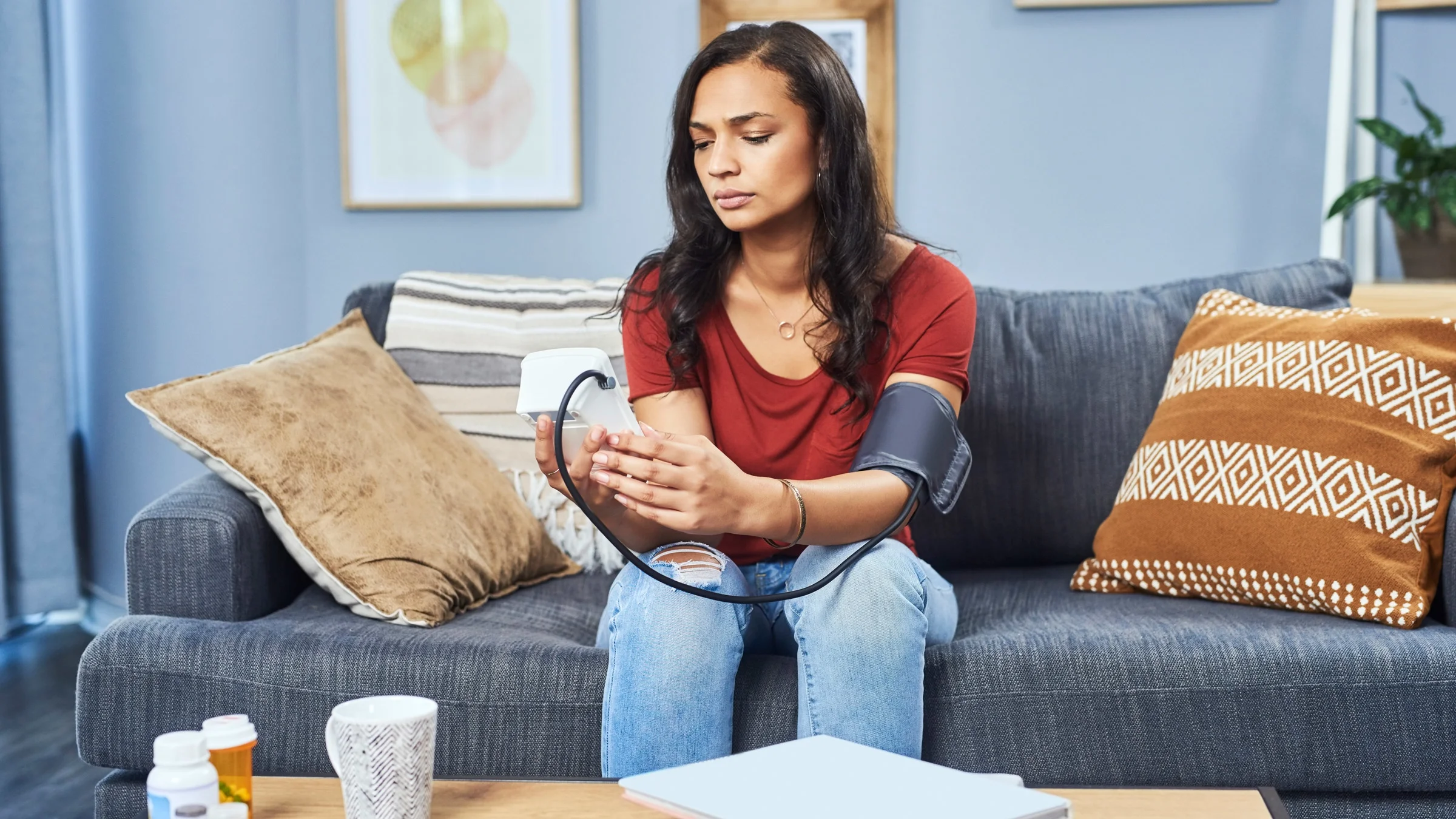 A person measuring their blood pressure in front of a table with pill bottles.