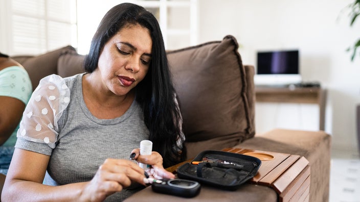 A Hispanic woman checks her blood sugar level at home.