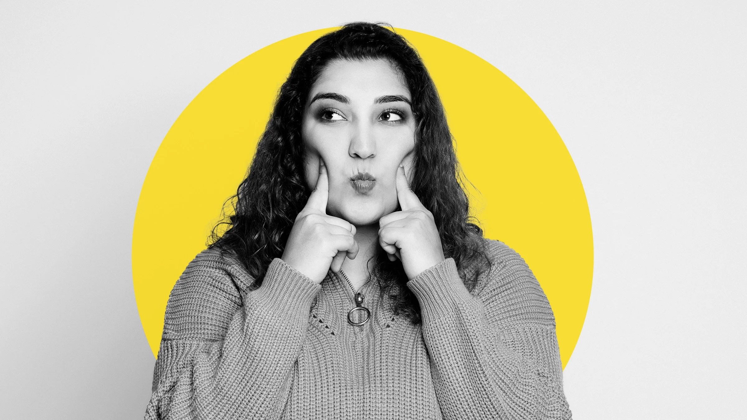 Black-and-white portrait of a woman sucking in her cheeks. There is an added yellow graphic circle behind her.