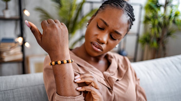 A Black woman with psoriasis is looking at a rash on her arm.