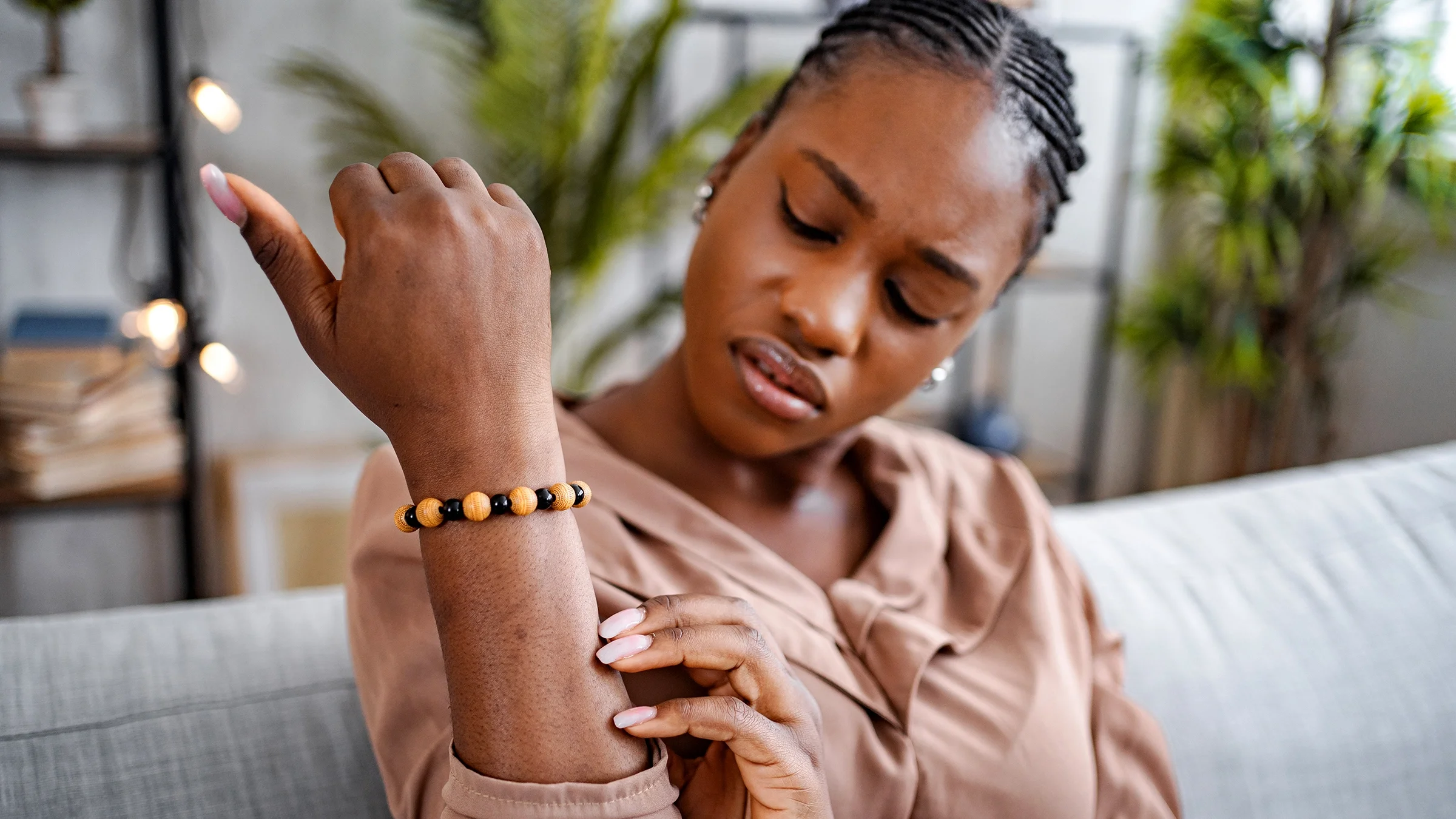 A Black woman with psoriasis is looking at a rash on her arm.