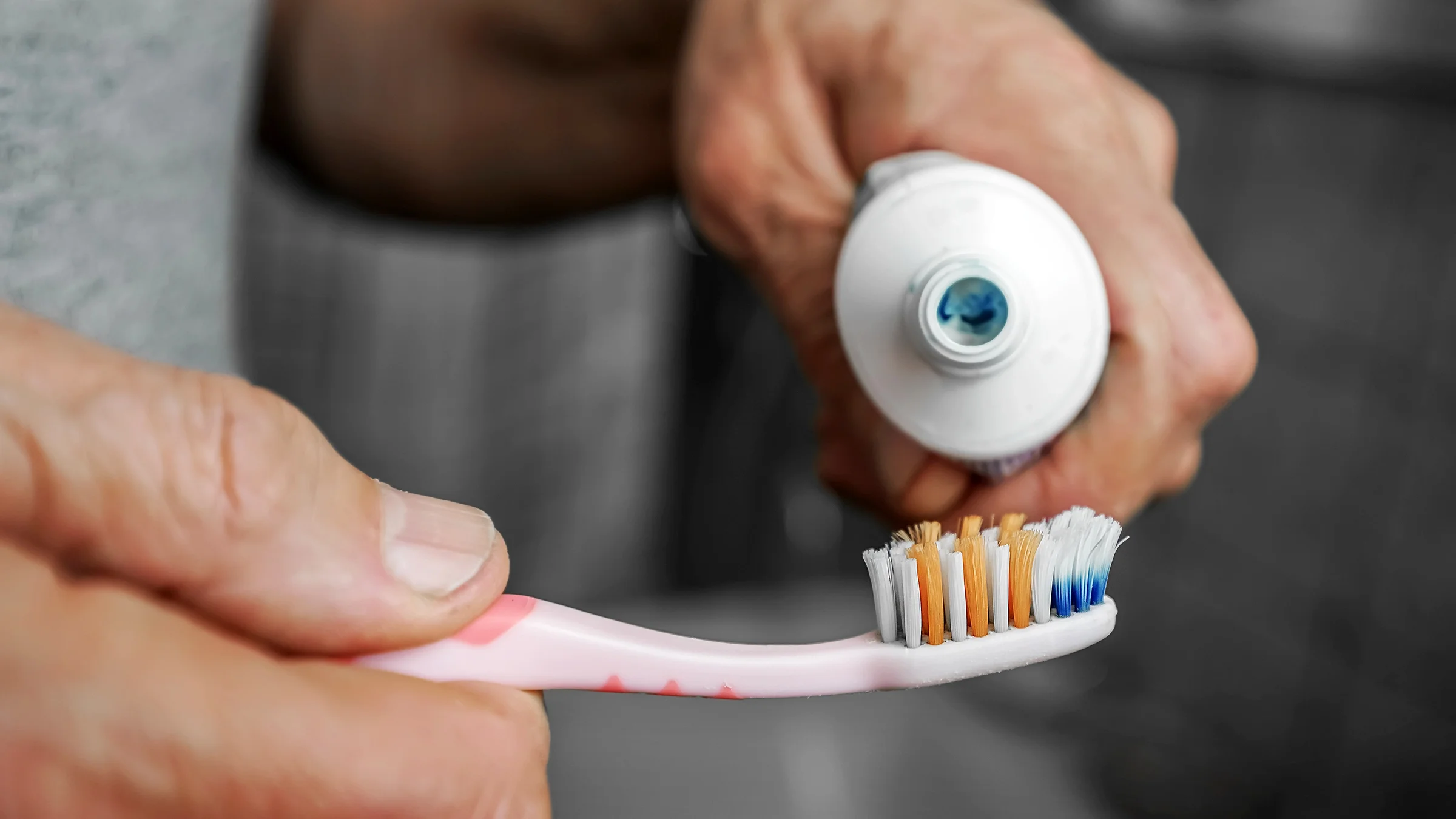 Close-up of a man holding a tube of toothpaste and a toothbrush.