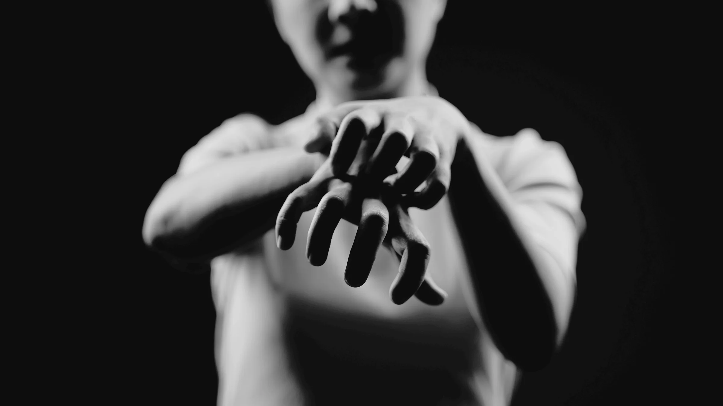 Black-and-white image of a person scratching their hands. The focus is on the hands with them in the background blurry. The primary color is the black background.