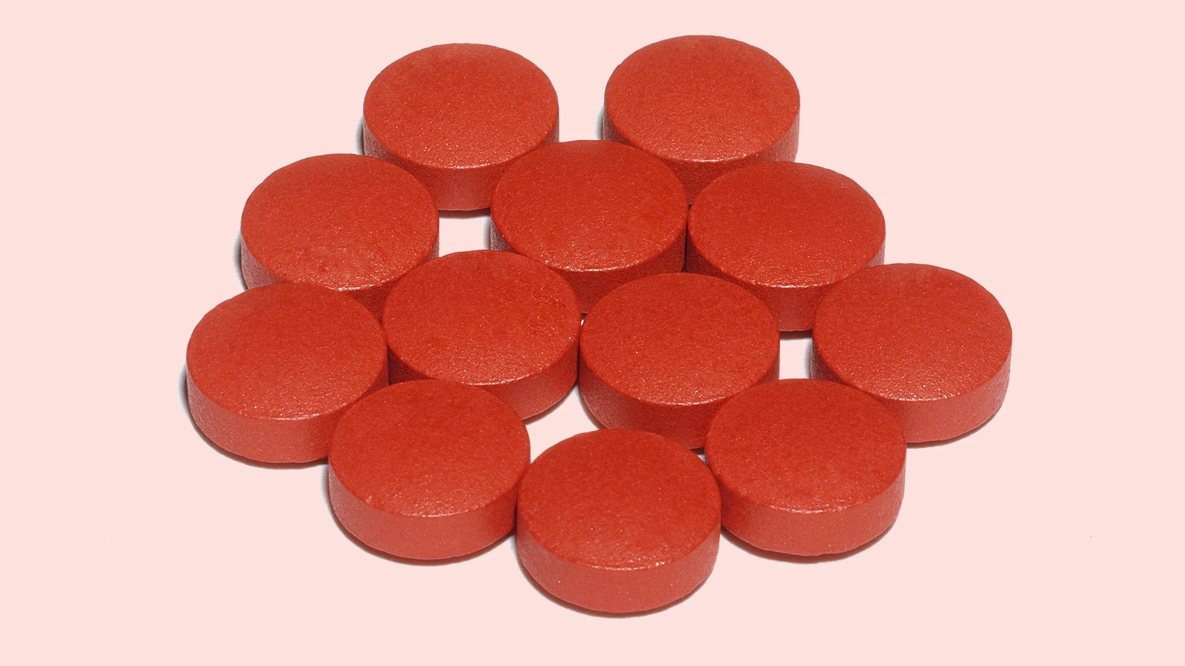 Pile of red Sudafed pills on a light pink background.