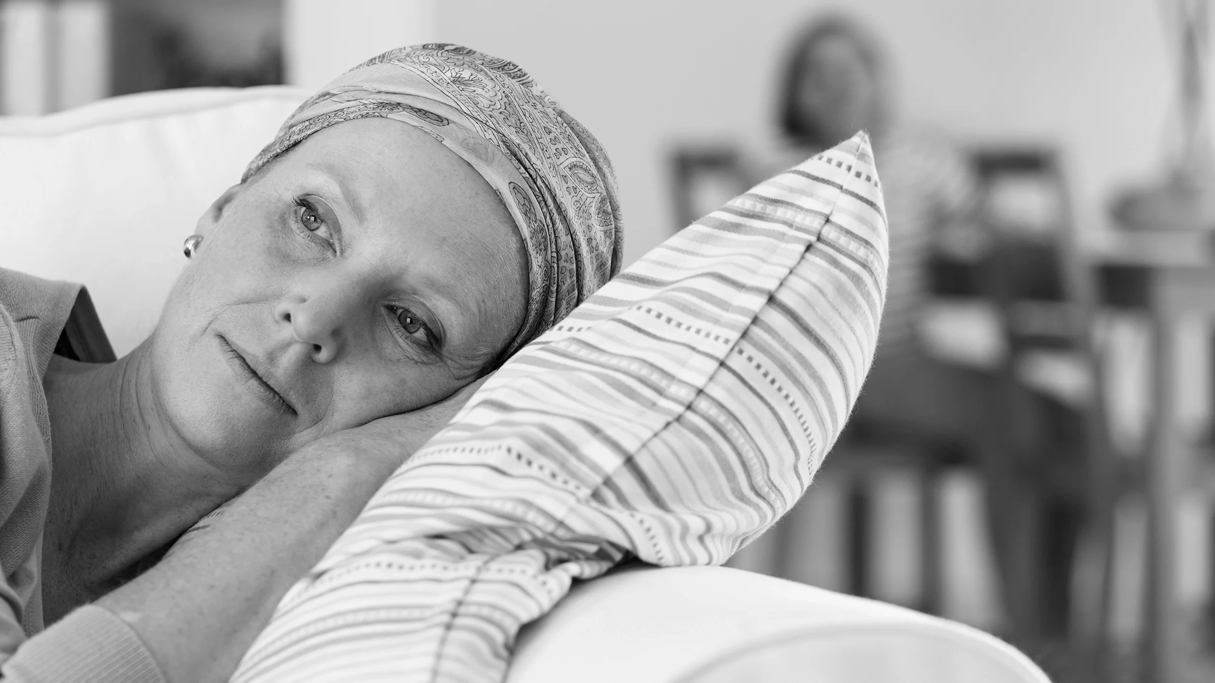 Black and white image of a woman laying on the couch with a sad expression. She is wearing a headscarf.