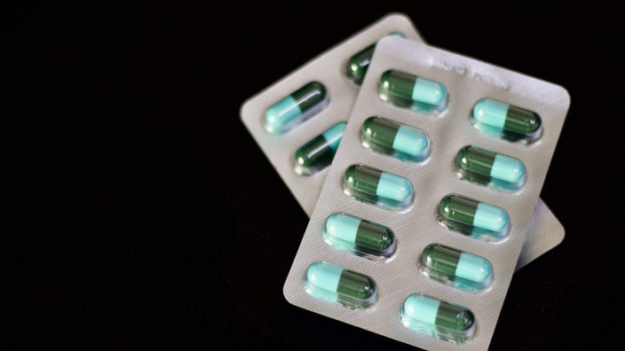 Blister packs of medication on a black background. The pills are green and teal inside the packs.