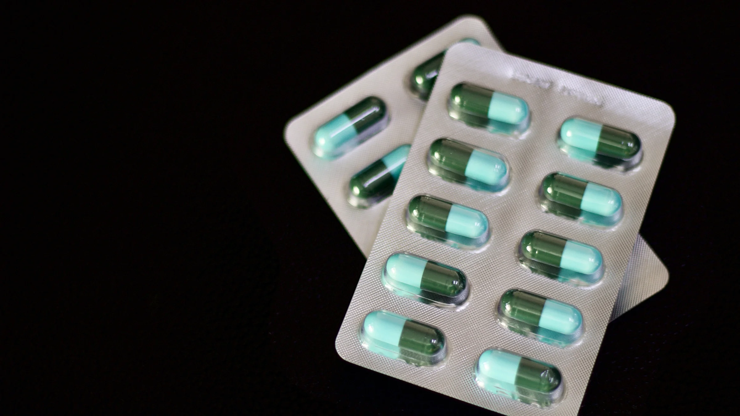 Blister packs of medication on a black background. The pills are green and teal inside the packs.