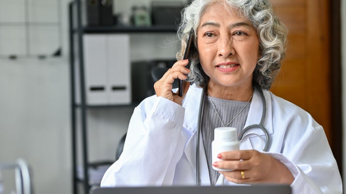 Pharmacist holding pill bottle and talking on phone.