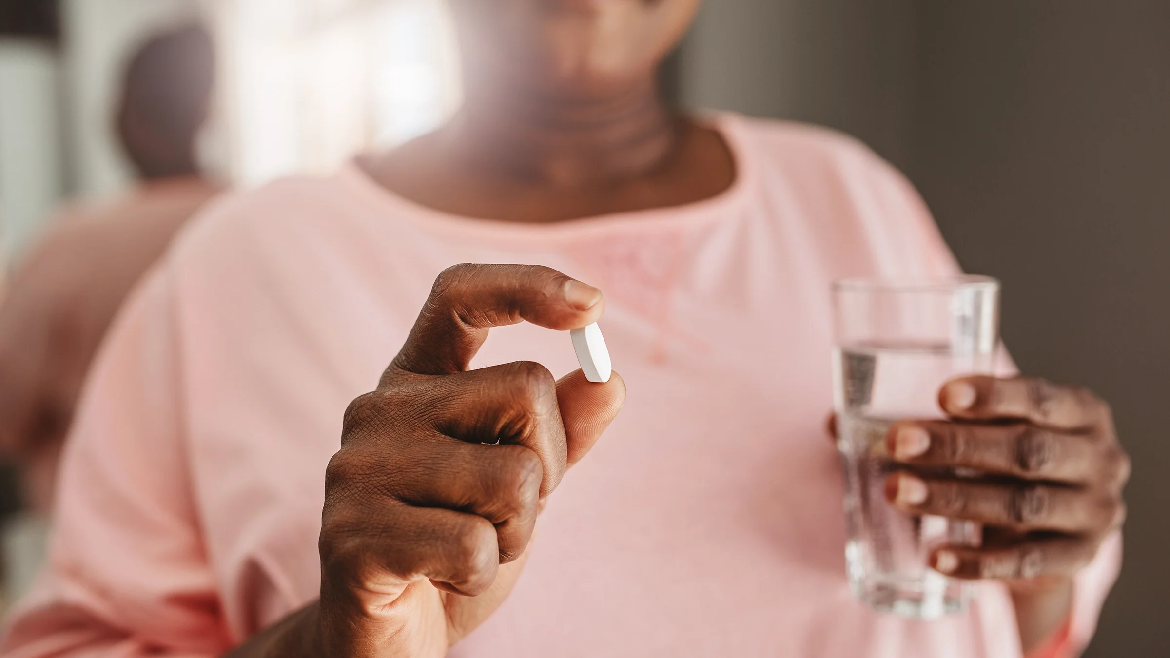 A woman holds a pill and a glass of water.