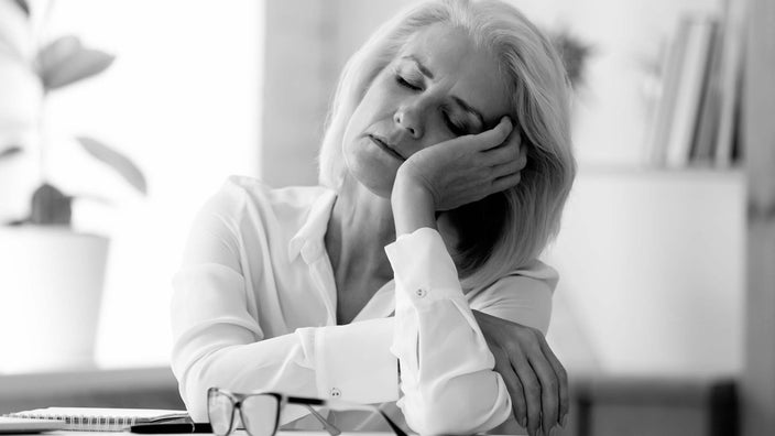 Black and white portrait of an older woman tired at her desk.